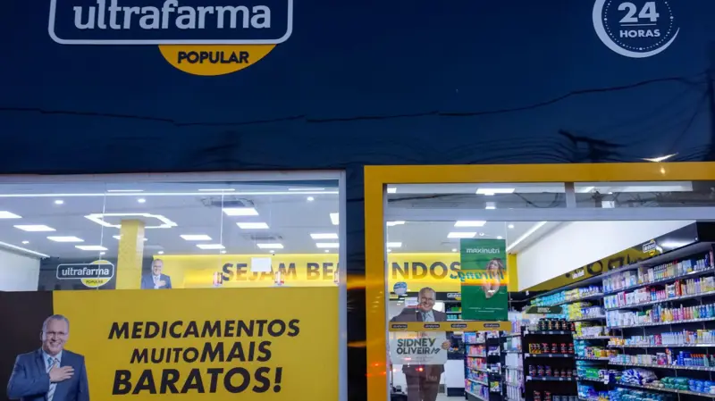 Fachada de uma loja Ultrafarma, com imagem de Sidney bem na frente e uma propaganda ''Medicamentos muito MAIS BARATOS''