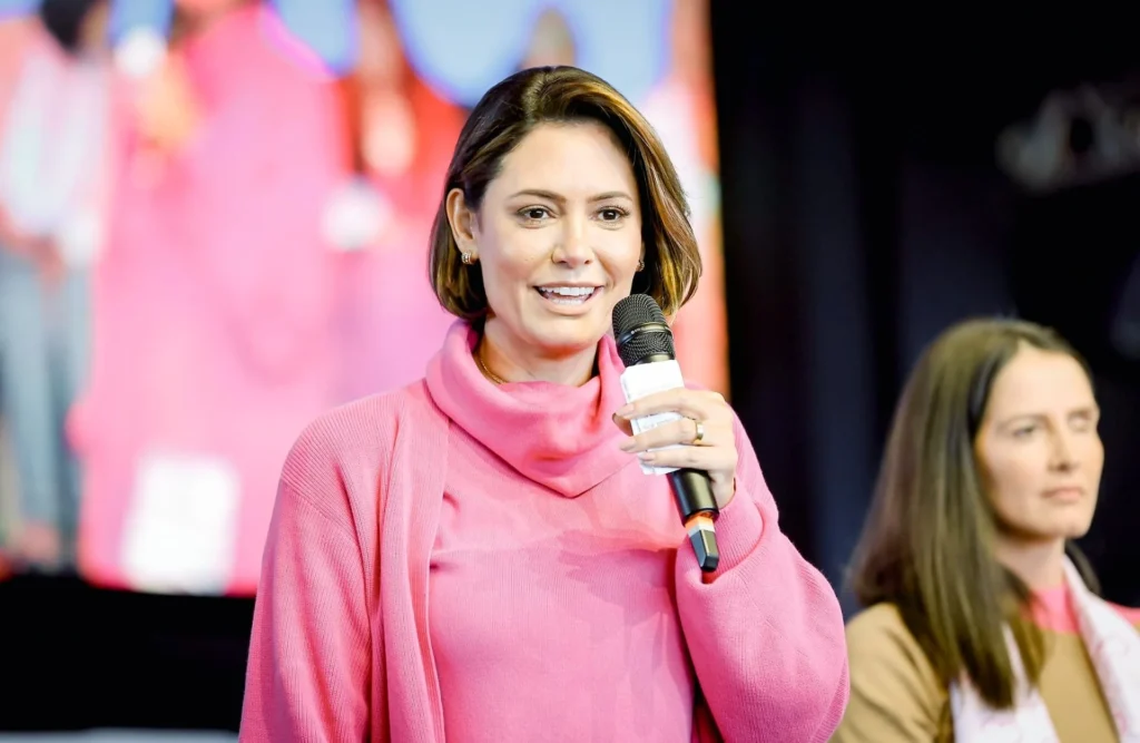 Michelle Bolsonaro, ex-primeira-dama do Brasil, falando ao microfone durante evento público, vestindo roupa rosa