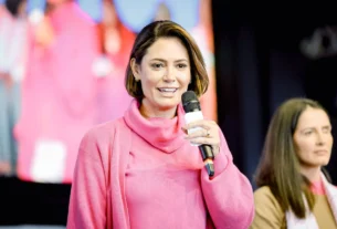 Michelle Bolsonaro, ex-primeira-dama do Brasil, falando ao microfone durante evento público, vestindo roupa rosa