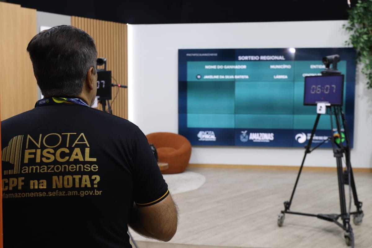 Imagem mostra servidor com a camisa da nota fiscal amazonense lendo um telão com nome de alguns sorteados - Nota Fiscal Amazonense Realiza 100º Sorteio com 600 Mil Inscritos